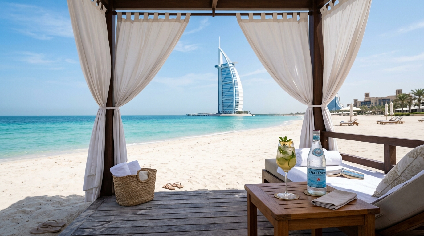 Jumeirahのプライベートビーチカバナ。白いカーテンが風に揺れている。木製テーブル、ターコイズブルーの海、白砂のビーチ、バックグラウンドのBurj Al Arab